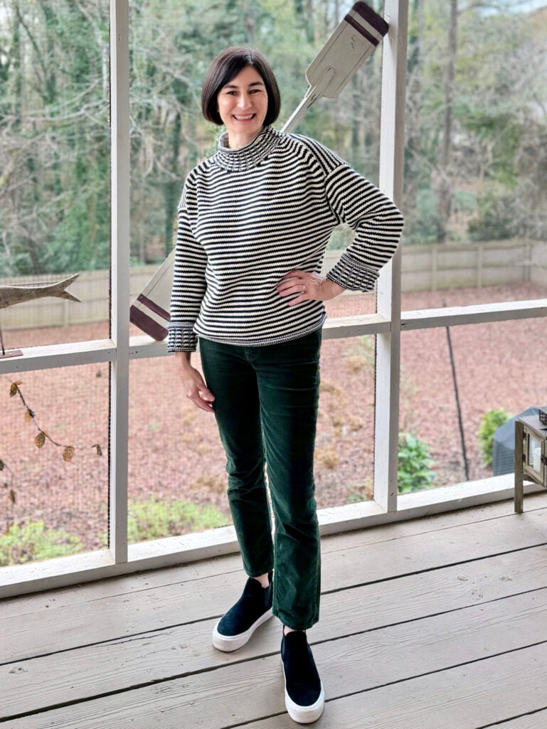 Kelly wearing a black and white striped turtleneck sweater, forest green velvet pants, and navy slip-on sneakers