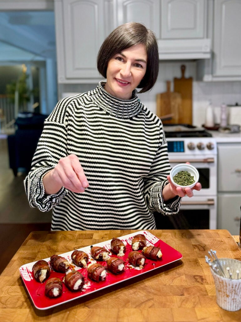 Kelly sprinkling fresh herbs over bacon-wrapped dates in the kitchen