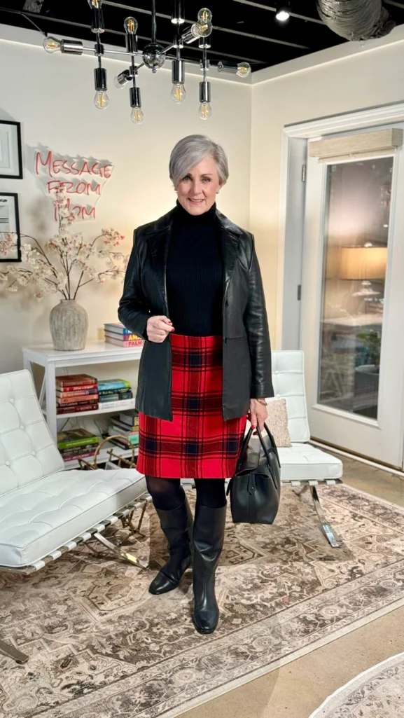 Beth wearing a red tartan A-line skirt with a black cashmere turtleneck, black leather blazer, black opaque tights, knee-high black boots, and black leather satchel—sophisticated holiday skirt outfit over 50