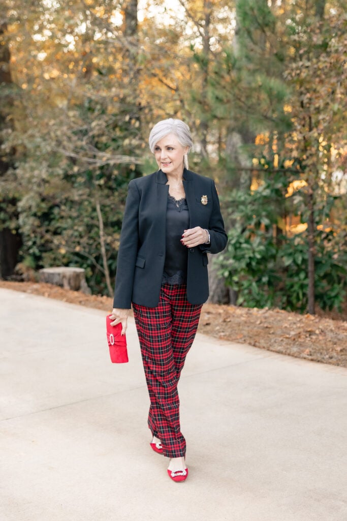 Beth in red tartan plaid pants paired with a black notched blazer, black lace-trim camisole, red suede pumps with crystal buckle, and matching red clutch—elegant holiday party outfit over 50