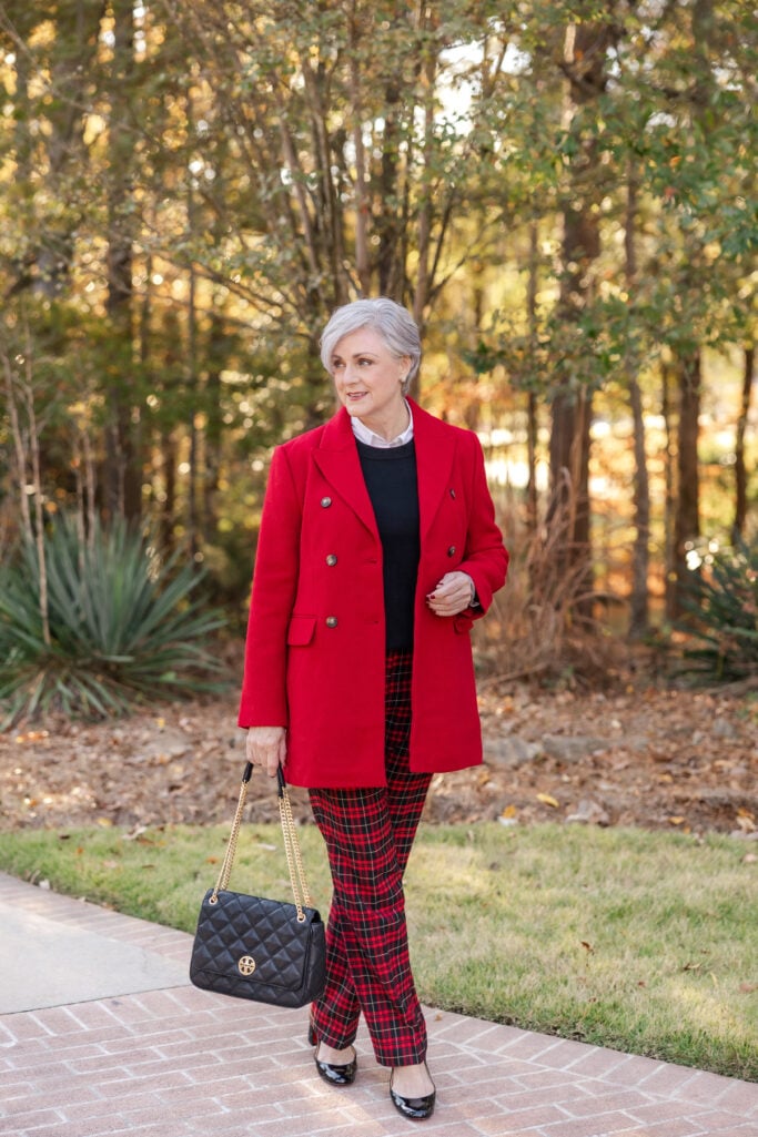 Beth styling tartan plaid pants with a bold red double-breasted coat, black cashmere crewneck, white button-down collar, black patent heels, and quilted black Tory Burch bag—festive holiday outfit over 50