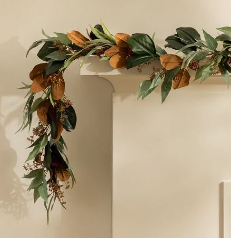 Magnolia and eucalyptus holiday garland with realistic green leaves, warm brown magnolia foliage, and subtle berry accents, draped over a mantel for natural seasonal décor.