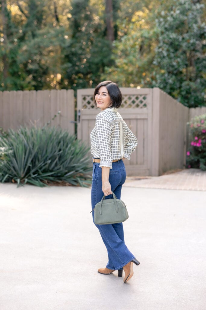 Woman over 40 wearing tan suede ankle boots with flare jeans and printed blouse