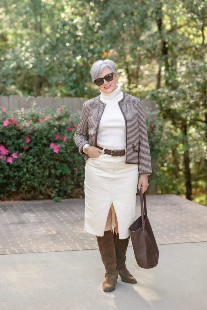 Woman over 50 styling brown suede knee-high boots with white denim skirt and houndstooth blazer