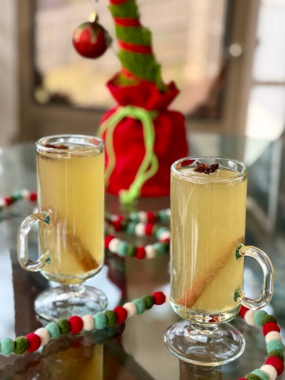 Two hot toddies garnished with cinnamon sticks and star anise, surrounded by festive red and green felt ball garland