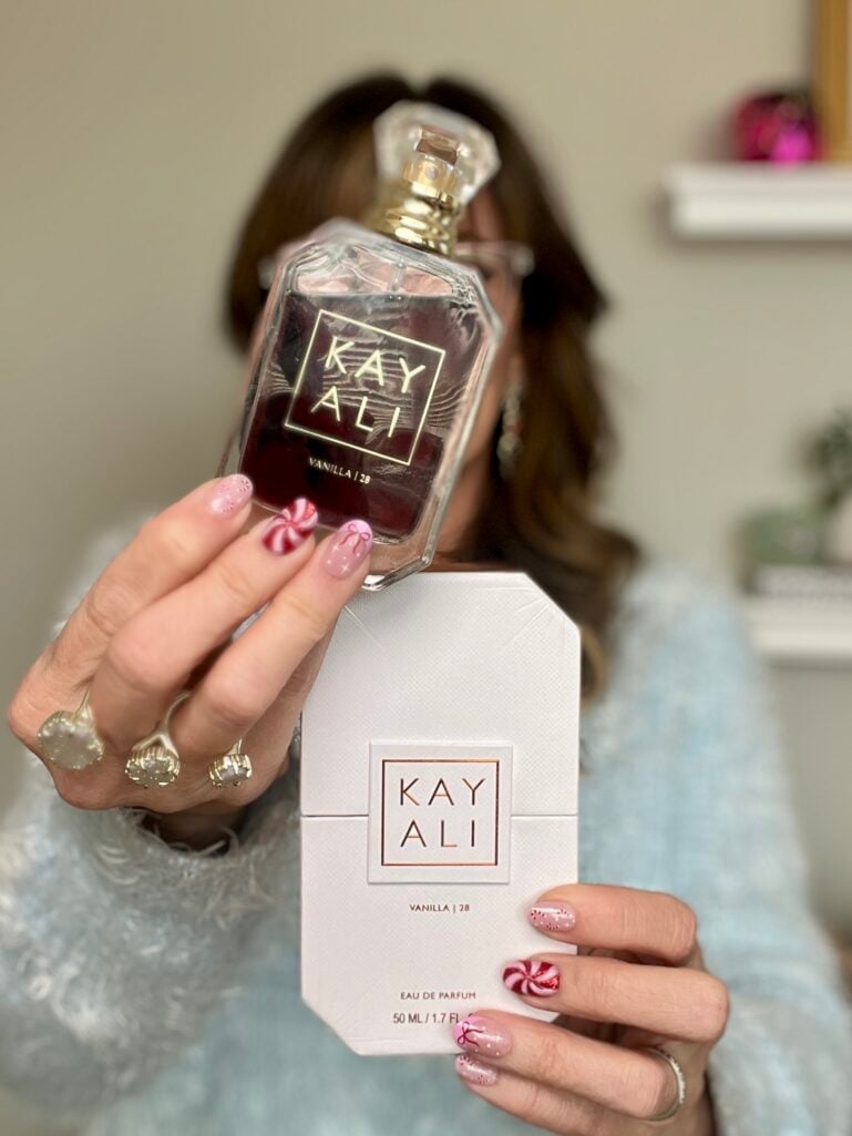 Hand holding Kayali Vanilla 28 eau de parfum bottle with candy cane nail art and product box