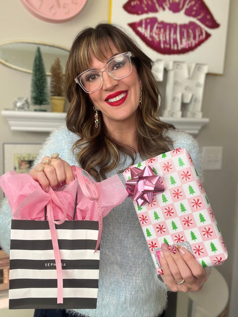 Woman in ice blue fuzzy sweater holding Sephora striped gift bag and wrapped present with peppermint and tree pattern wearing candy cane nails
