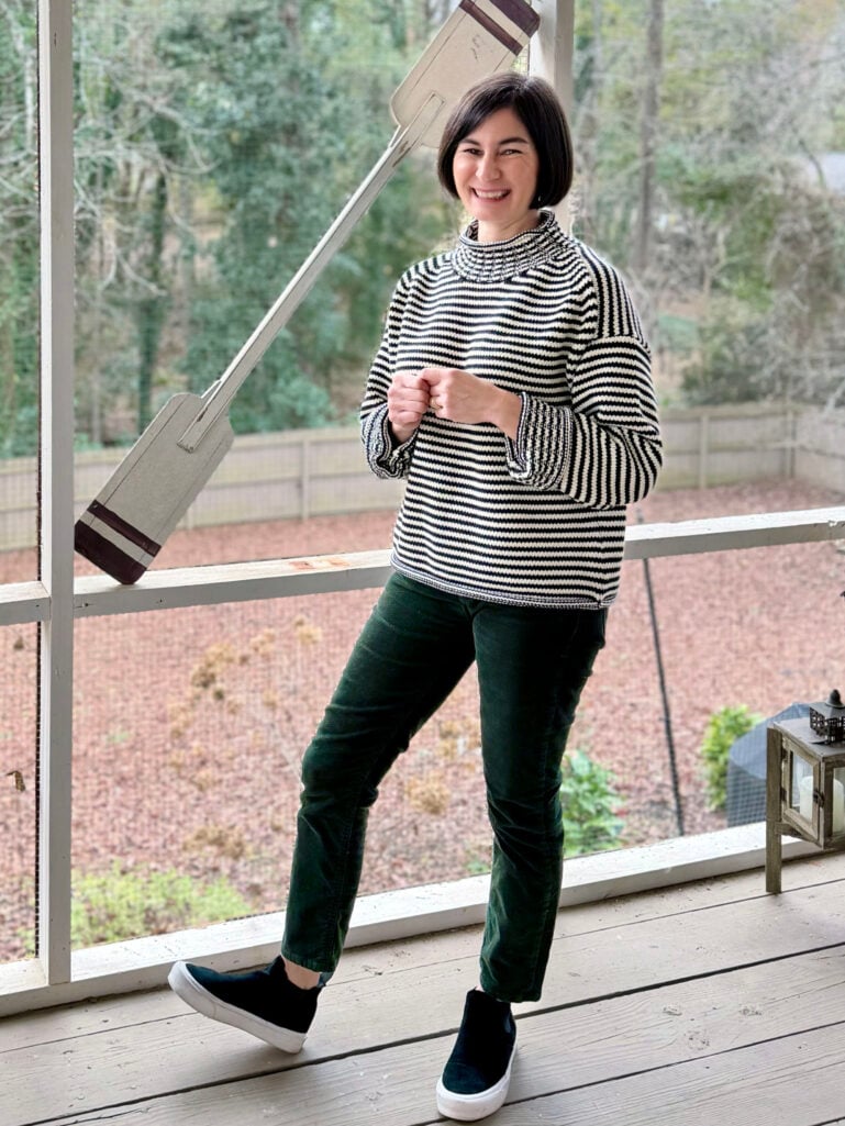 Kelly smiling in her striped turtleneck and green corduroy pants on the screened porch