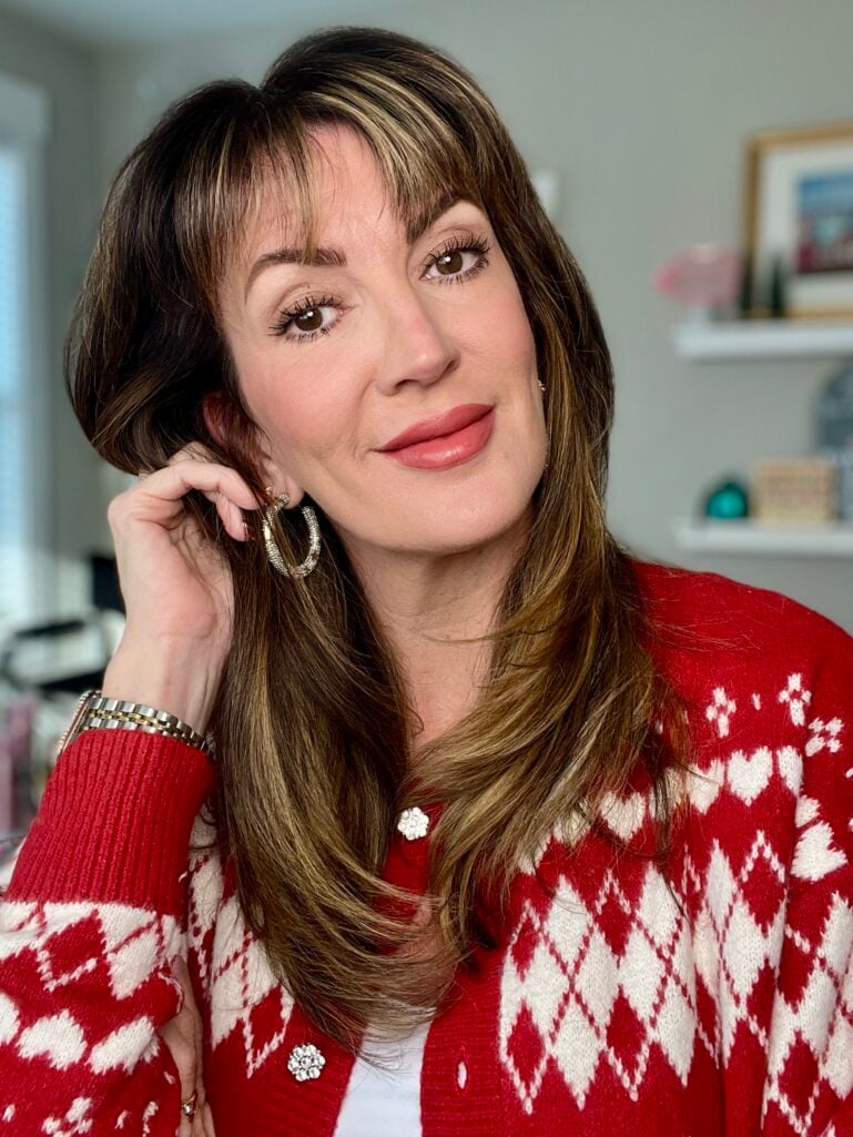 Woman with natural makeup look wearing red and white holiday cardigan with rhinestone buttons and gold star hoop earrings