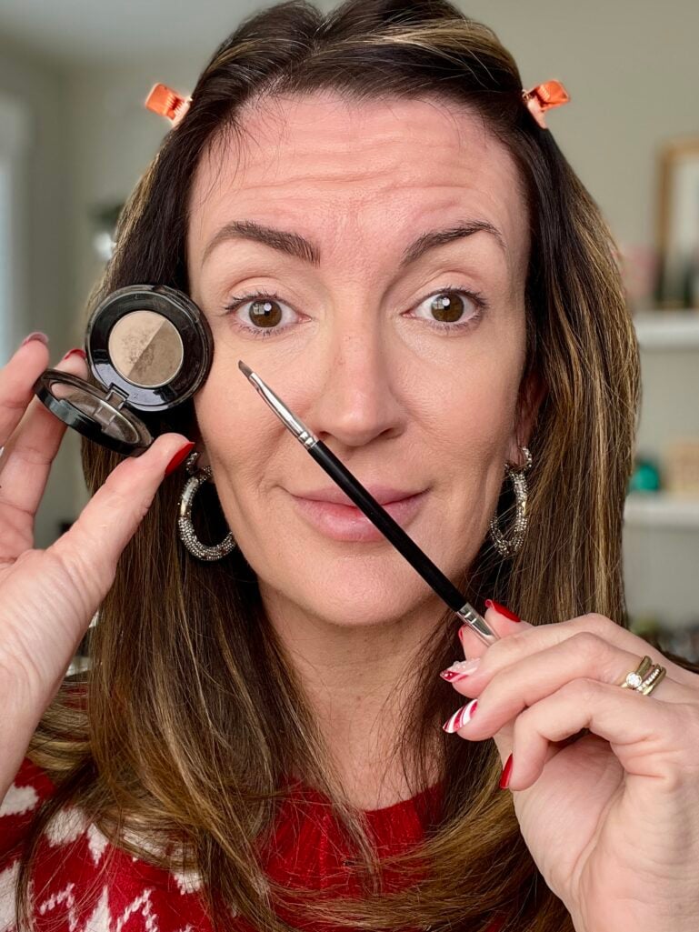 Woman holding Anastasia Beverly Hills brow powder duo and angled brow brush showing filled-in eyebrows with hair clipped back