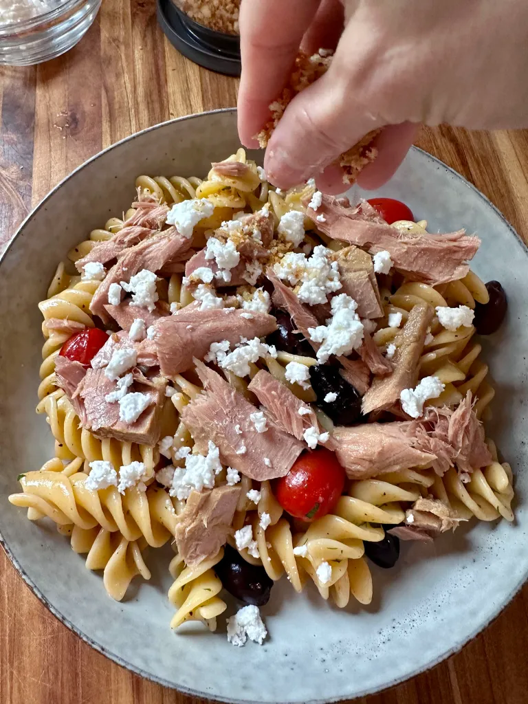 Hand sprinkling toasted panko breadcrumbs over the finished pasta