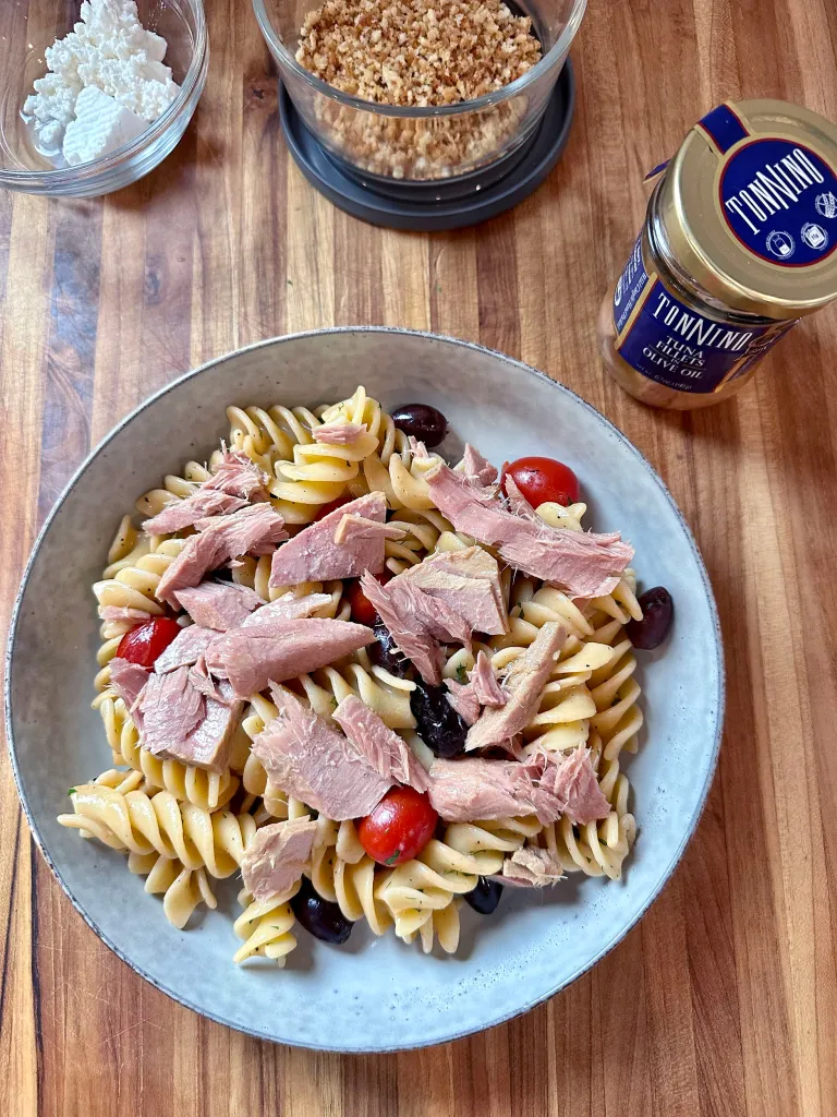 Arranging Tonnino tuna fillets on top of the Greek pasta with feta and breadcrumbs in the background