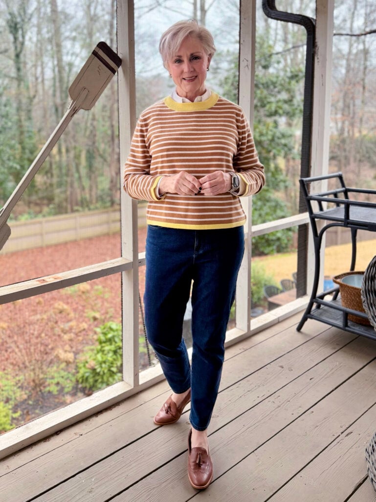 Full-length view of Beth in her striped sweater and jeans, hands clasped, winter trees visible through the porch screens