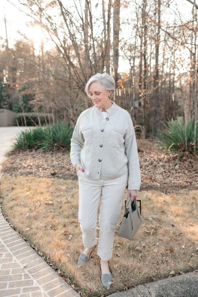 Woman over 60 wearing a soft neutral cardigan jacket, winter white trousers, and flats outdoors