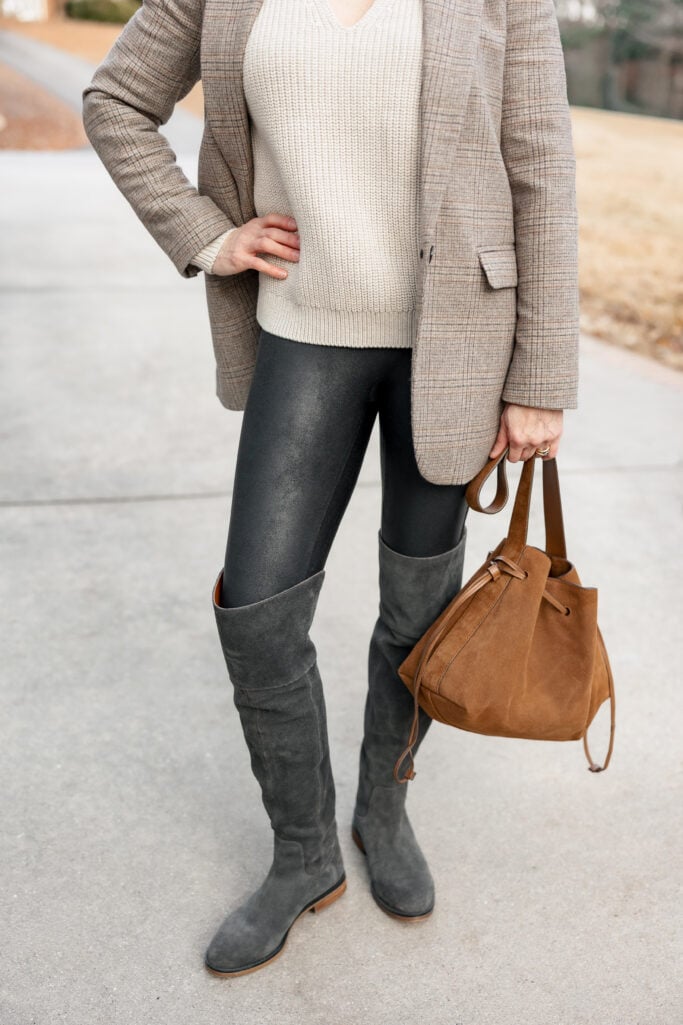 Detail shot of petite outfit showing plaid blazer, cream V-neck sweater, Spanx faux leather leggings, grey suede tall boots and tan suede drawstring bag