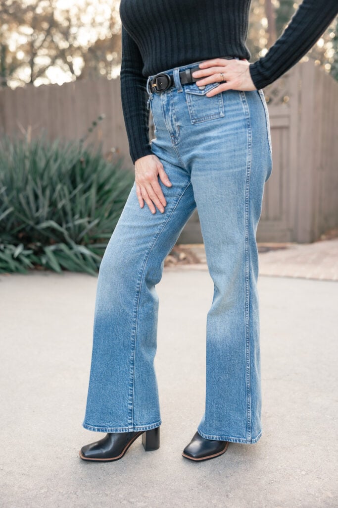 elly wearing petite wide leg trouser jeans with black ribbed turtleneck, black belt, and black heeled boots - detail view of the jeans