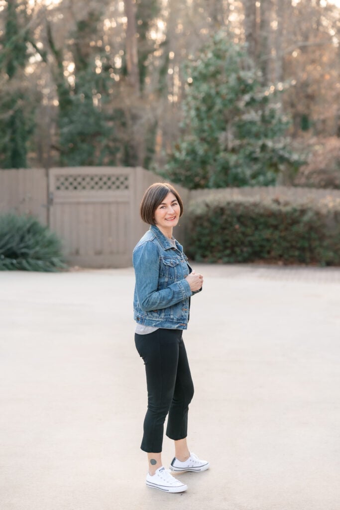 Kelly in petite casual outfit from side angle showing denim jacket length and black ponte pant fit with white Converse sneakers