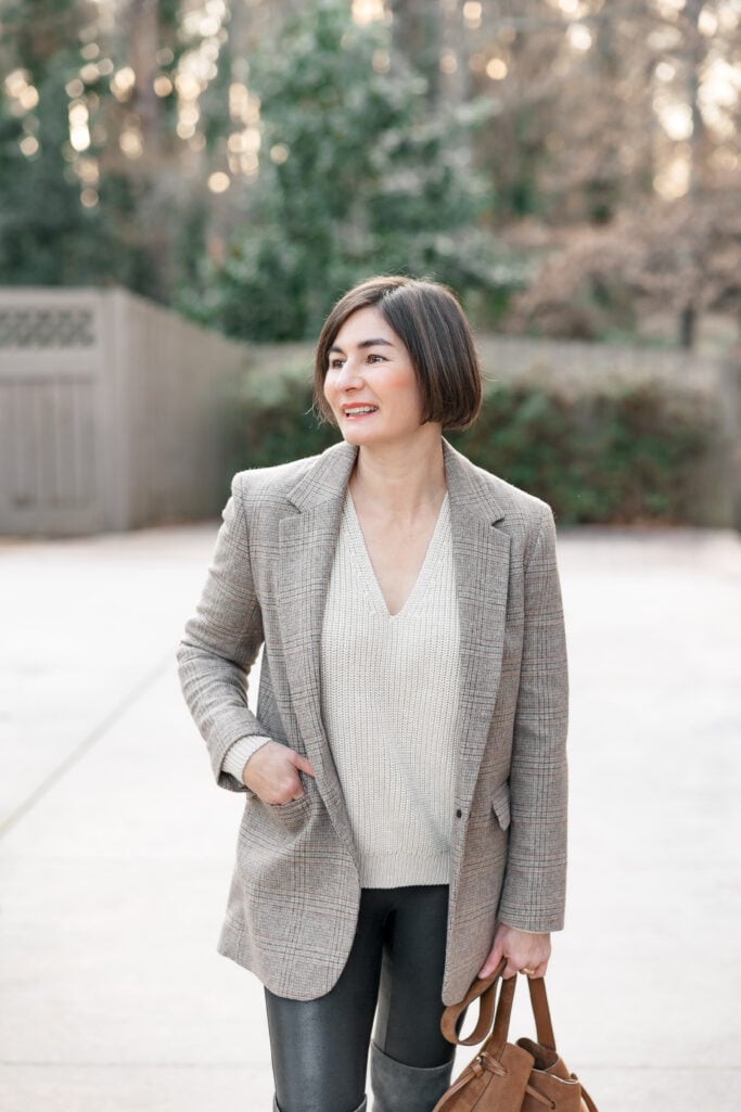 Kelly in elevated petite leggings outfit with plaid Madewell blazer, cream V-neck fisherman sweater, and faux leather leggings - upper body shot with tan suede bag