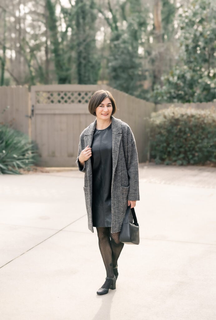 Kelly wearing black faux leather mini sheath dress with grey plaid knit coatigan, herringbone tights, and black woven block heel pumps - full length petite outfit showing dress length hitting above the knee