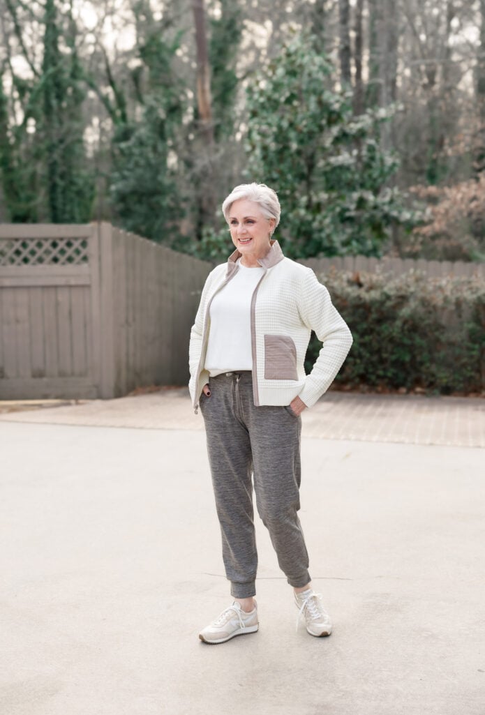 Woman over 50 wearing heather gray drawstring joggers with cream waffle-knit jacket and white tee, styled with neutral sneakers for an elevated athleisure look