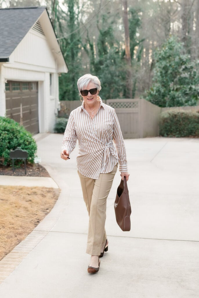Beth Djalali wears a tan-and-white striped tie-front shirt with khaki pants, brown slingback heels, and a brown tote.