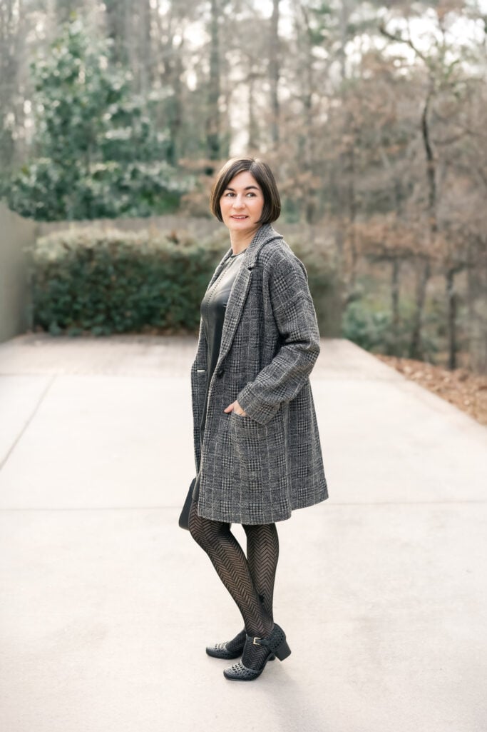 Kelly in full length side view wearing faux leather sheath dress with long grey plaid knit jacket and patterned tights - petite winter dress styling
