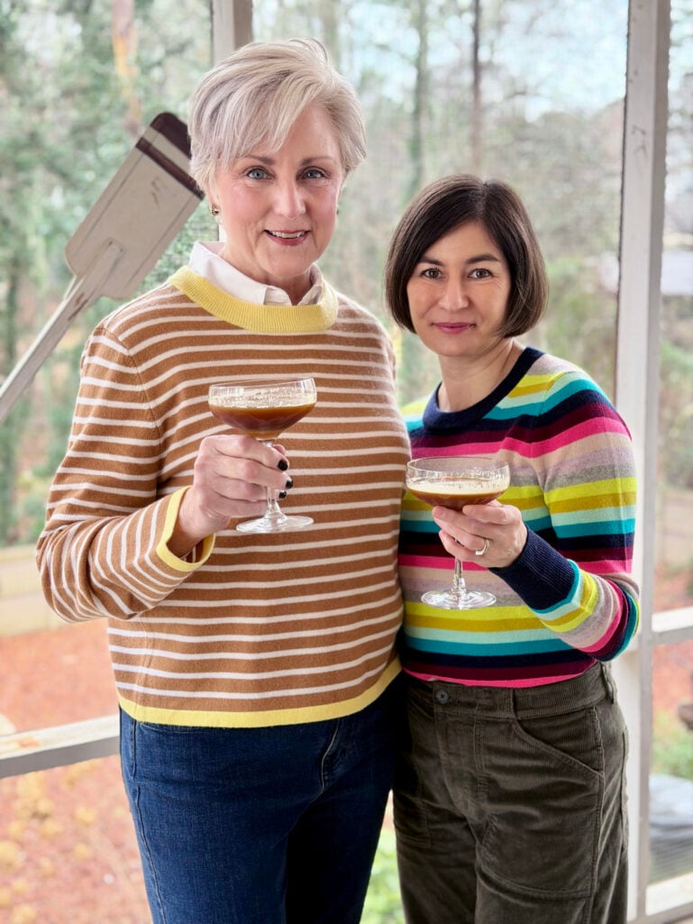 Beth and Kelly raising their Salted Caramel Espresso Martinis in a toast, both wearing their striped sweaters on the screened porch