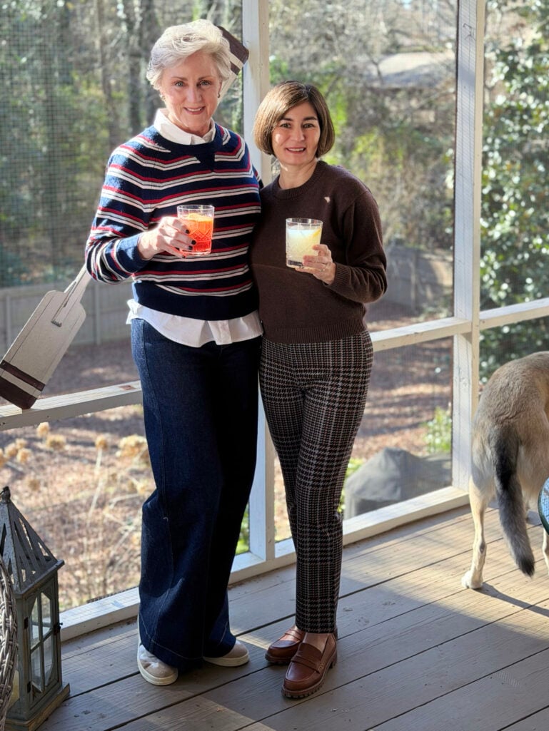 Beth and Kelly raising Aplos mocktails on the screened porch, with Oscar photobombing in the background, showing their full outfits