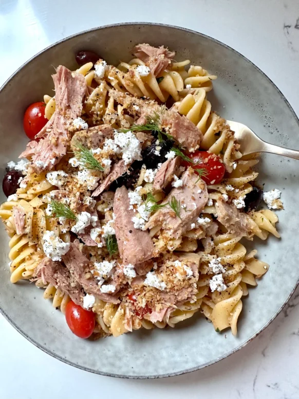 Greek pasta with tuna, feta, olives, and fresh dill in a gray speckled bowl with a fork