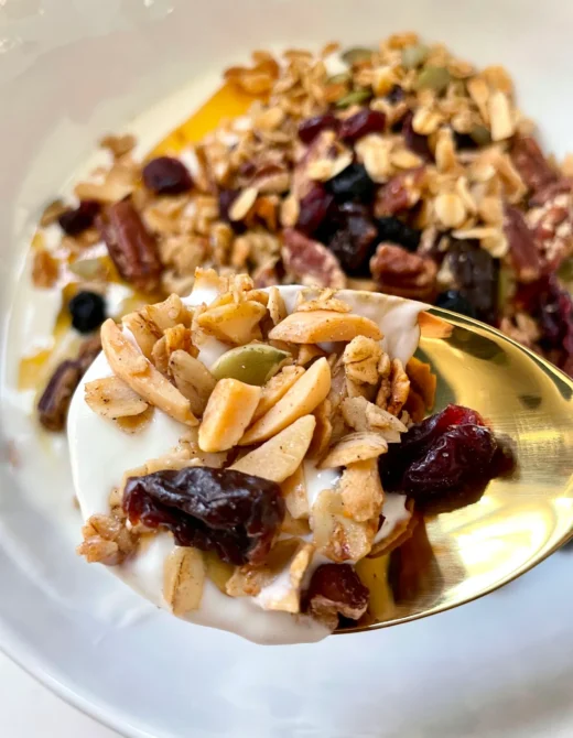 Spoonful of homemade granola with yogurt, dried cherries, cranberries, and almonds on a gold spoon