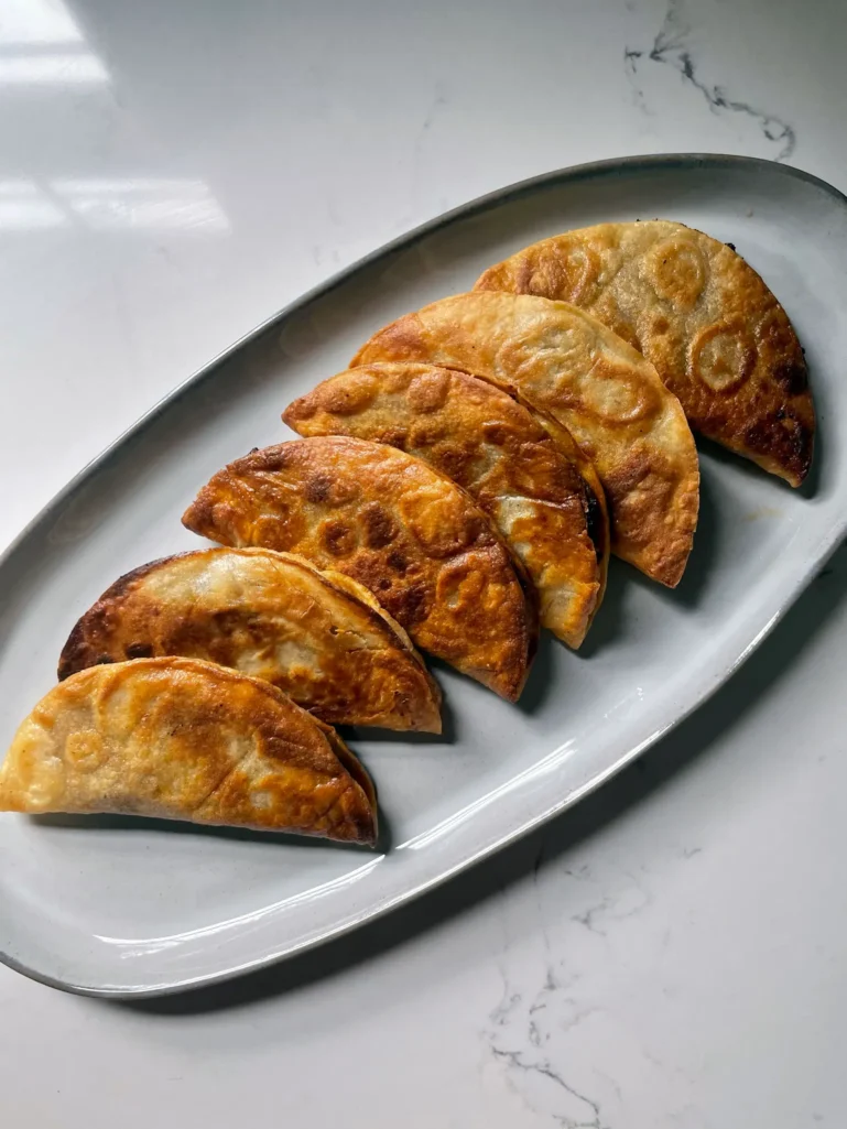 Six crispy tacos dorados arranged on an oval white platter