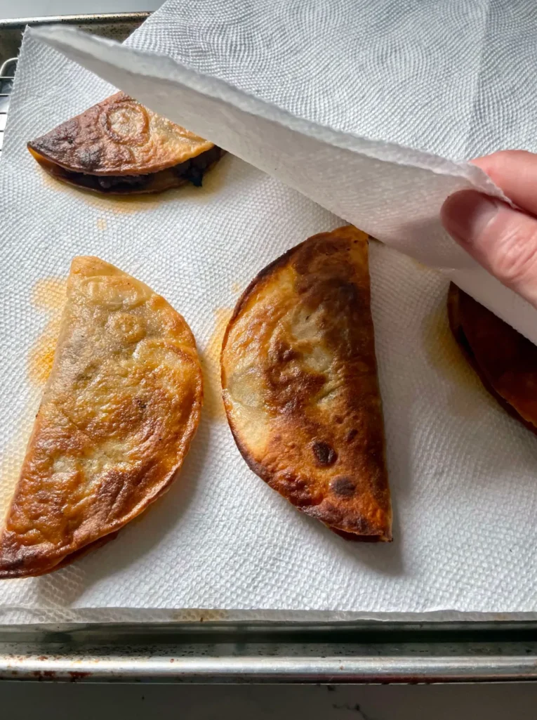 Blotting crispy fried tacos with paper towels on a wire rack