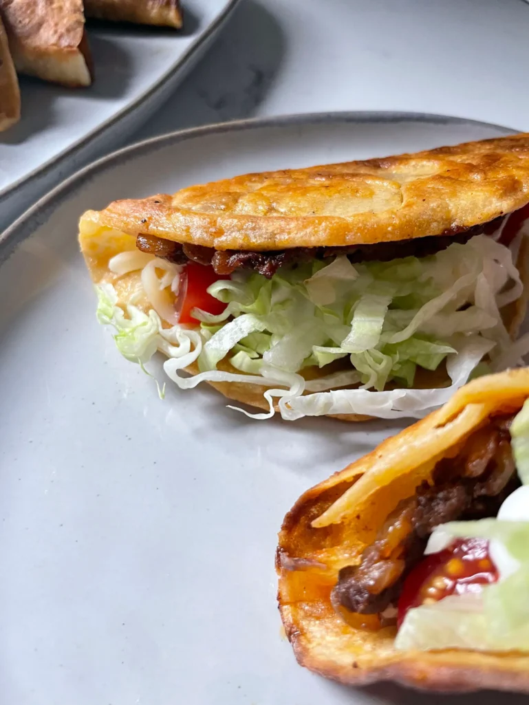 Close-up of two assembled crispy tacos with lettuce, tomato, cheese, and sour cream on a plate