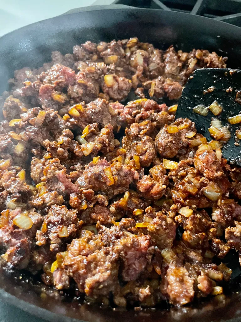 Seasoned ground beef cooking with onions in a cast iron skillet