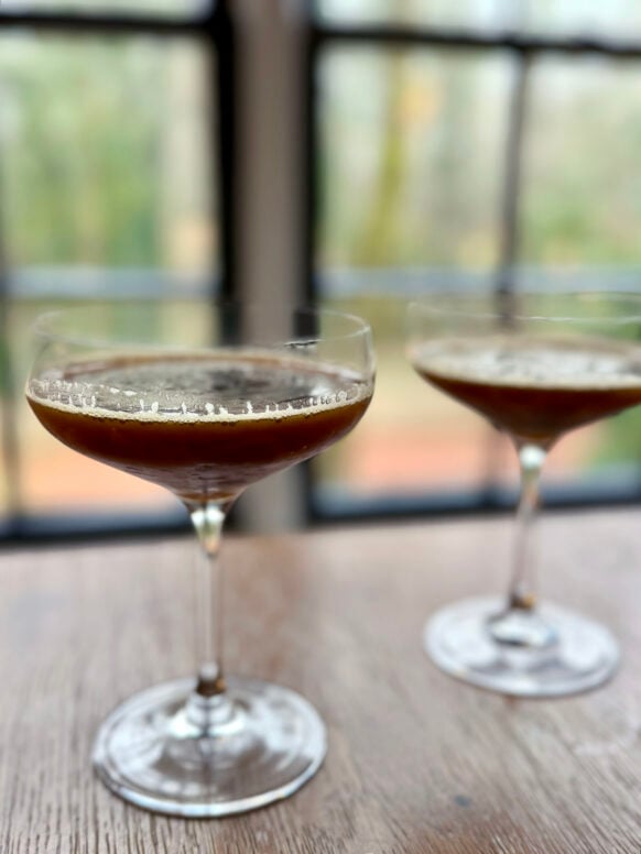 Two Salted Caramel Espresso Martinis in coupe glasses on a wooden table, rich and frothy with soft light through the windows