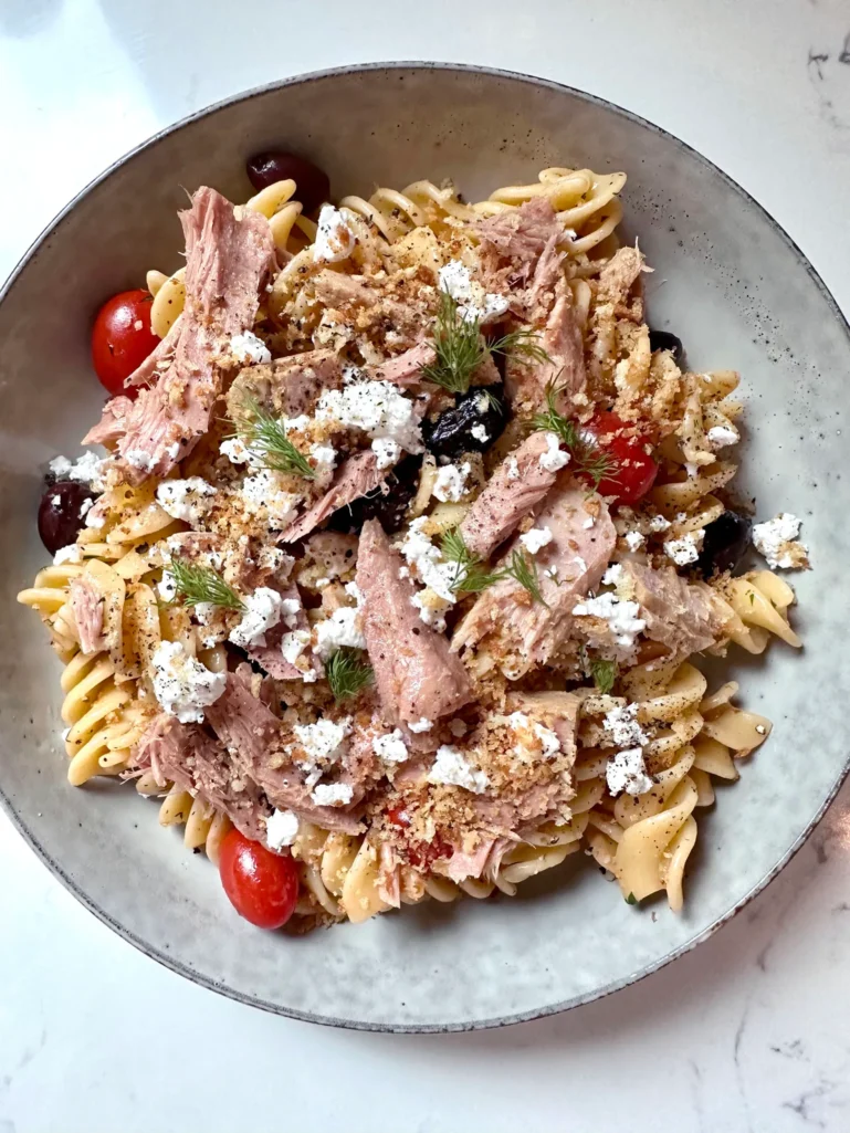 Overhead view of completed Greek pasta topped with tuna, feta, breadcrumbs, and dill fronds