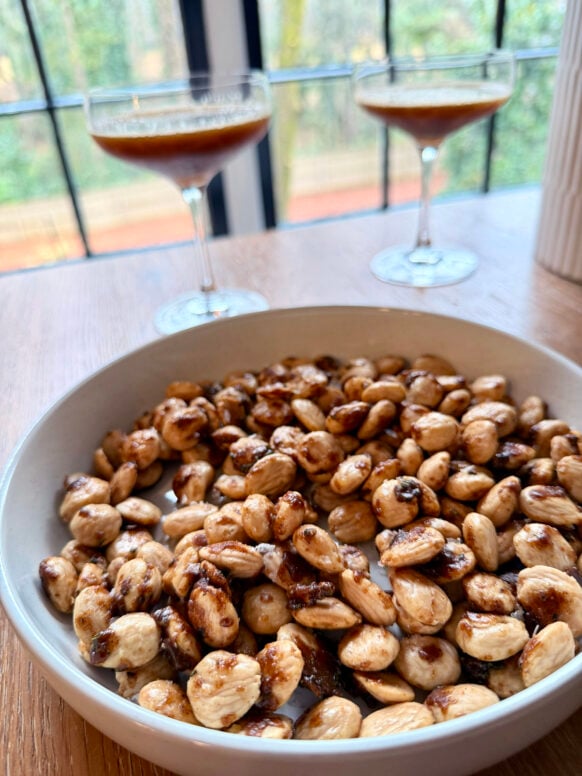A bowl of Spiced Marcona Almonds with caramelized brown sugar coating, two espresso martinis in the background