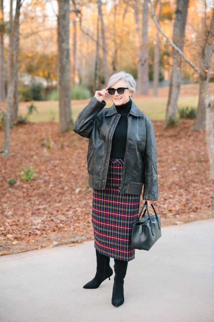 Woman over 50 in black fitted ribbed turtleneck sweater layered under leather jacket with leopard print pants and sunglasses