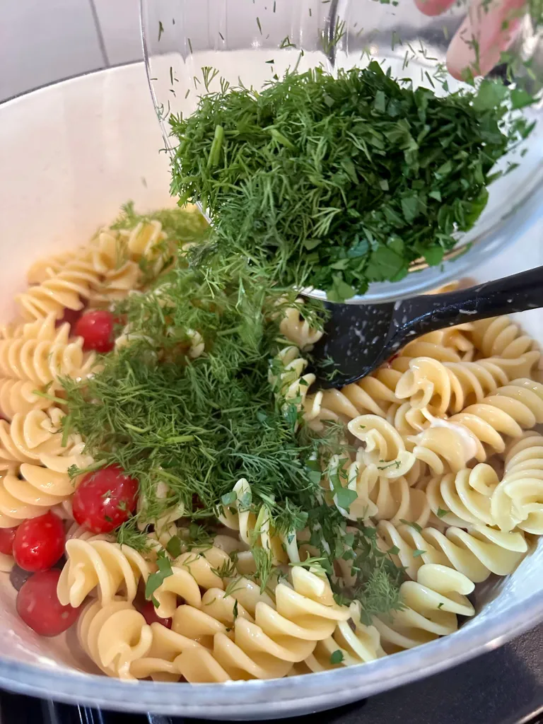 Pouring chopped fresh dill and parsley into the pasta pot