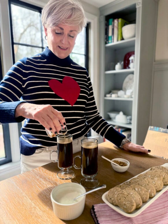 Beth pouring Jameson into two Irish Coffee glasses, a bowl of lightly whipped cream and a platter of shortbread cookies beside her