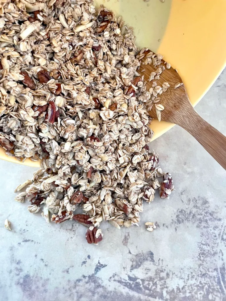 Pouring unbaked granola mixture from yellow bowl onto a sheet pan