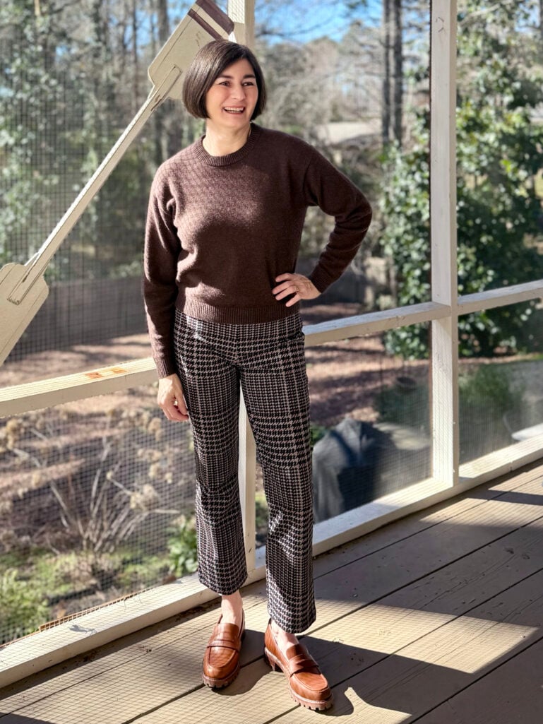 Kelly wearing a dark brown cashmere crewneck sweater, brown and black houndstooth ponte pants, and cognac penny loafers on the screened porch