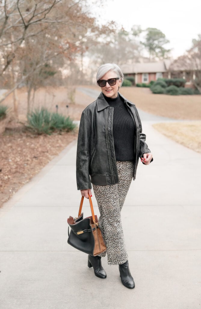 Woman over 50 in gray ribbed mock neck sweater dress styled with colorful silk scarf and burgundy boots