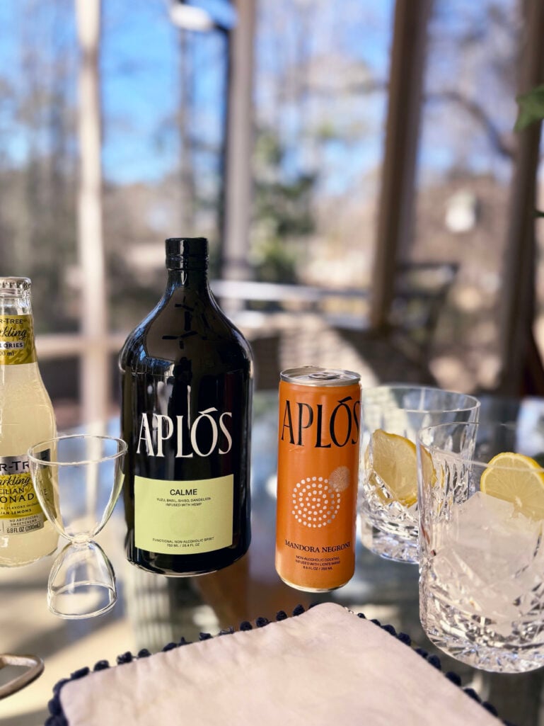 Aplos mocktail ingredients including Aplos Calme bottle, Aplos Mandora Negroni can, Fever-Tree Sparkling Sicilian Lemonade, and crystal rocks glasses with ice and lemon