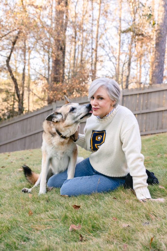 Oscar the German Shepherd giving Beth a kiss on the cheek as she sits with him in the backyard, golden autumn light in the background