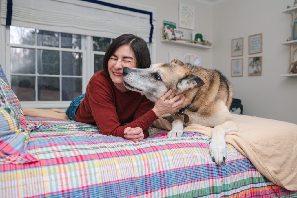 Kelly and Oscar sharing a tender moment on the bed, Kelly smiling with eyes closed as Oscar nuzzles close