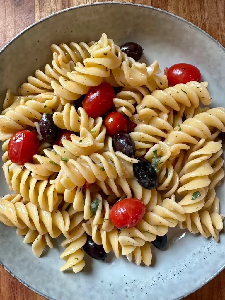 Fusilli pasta tossed with tomatoes, olives, and herbs in a gray speckled serving bowl