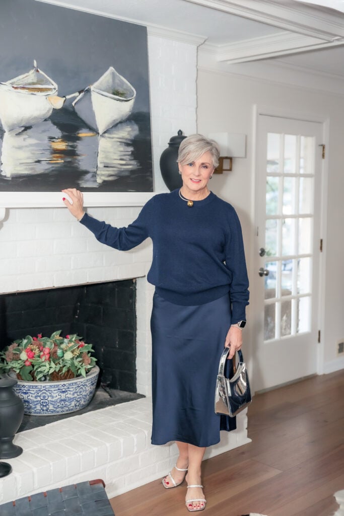 Beth Djalali in head-to-toe navy cashmere sweater and satin midi skirt with pearl necklace gold pendant and silver metallic bag
