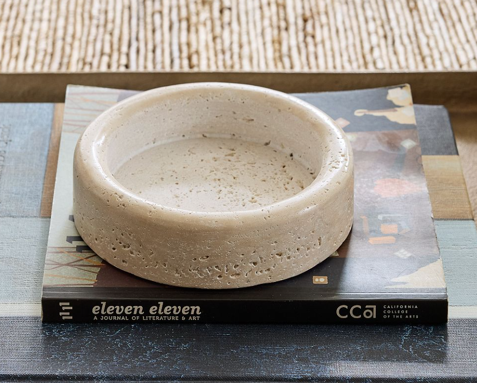 Round travertine stone catchall bowl with natural pitting, styled on stacked books as a decorative tabletop accent.