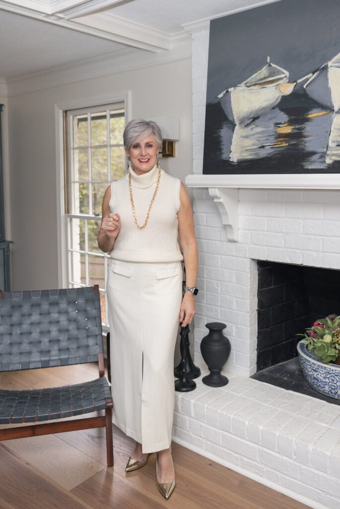 Woman over 50 wearing cream sleeveless turtleneck with gold chain necklace and wide-leg cream pants in monochromatic outfit